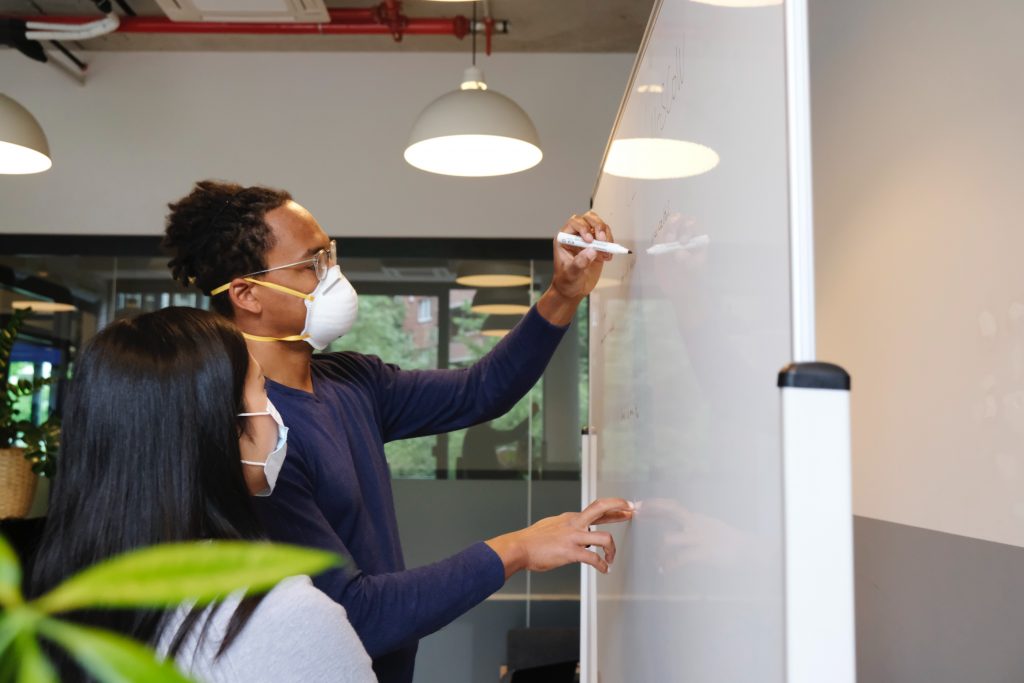 two coworkers in face masks planning on a whiteboard