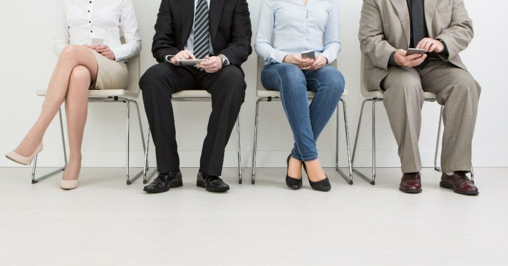 Four people sitting in a row of chairs, waiting with their hands in their laps.